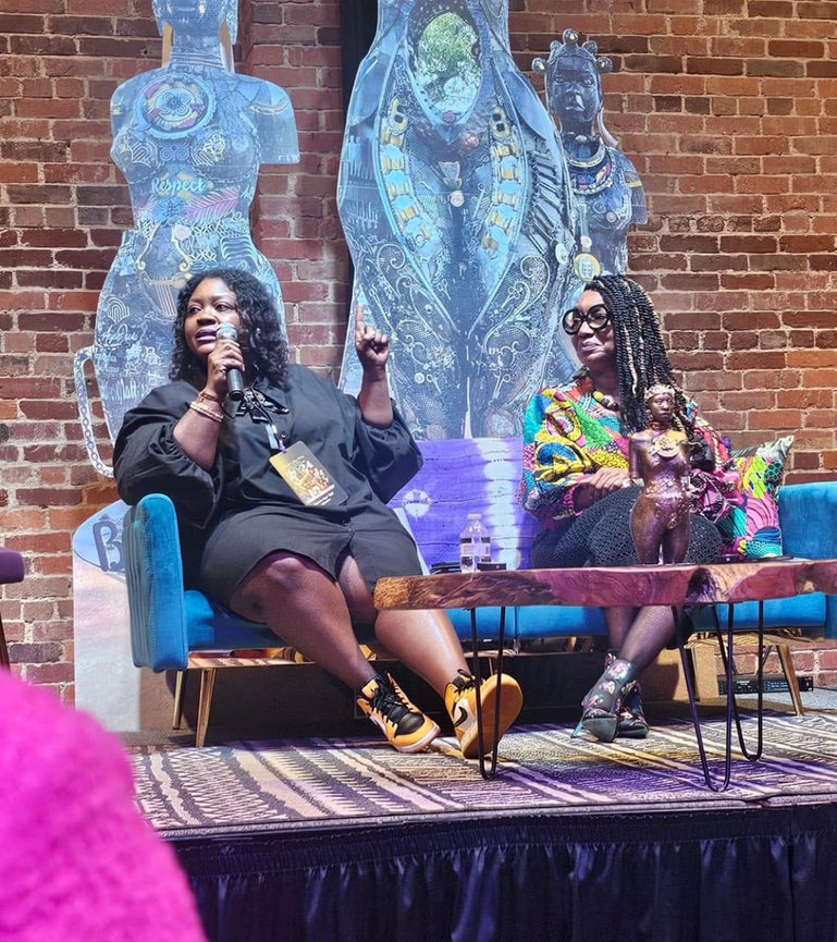 Two women seated on a stage during a panel discussion with a colorful artwork backdrop.