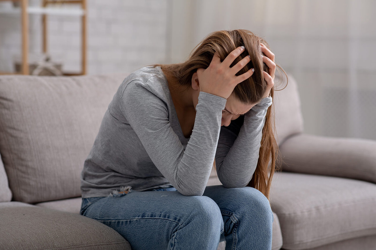 A woman holds her head in her hands while appearing upset on a couch. This could represent the pain that online trauma therapy in Texas can address. Contact a trauma therapist in Austin, TX to learn more about family trauma therapy in Austin, TX and other services. 